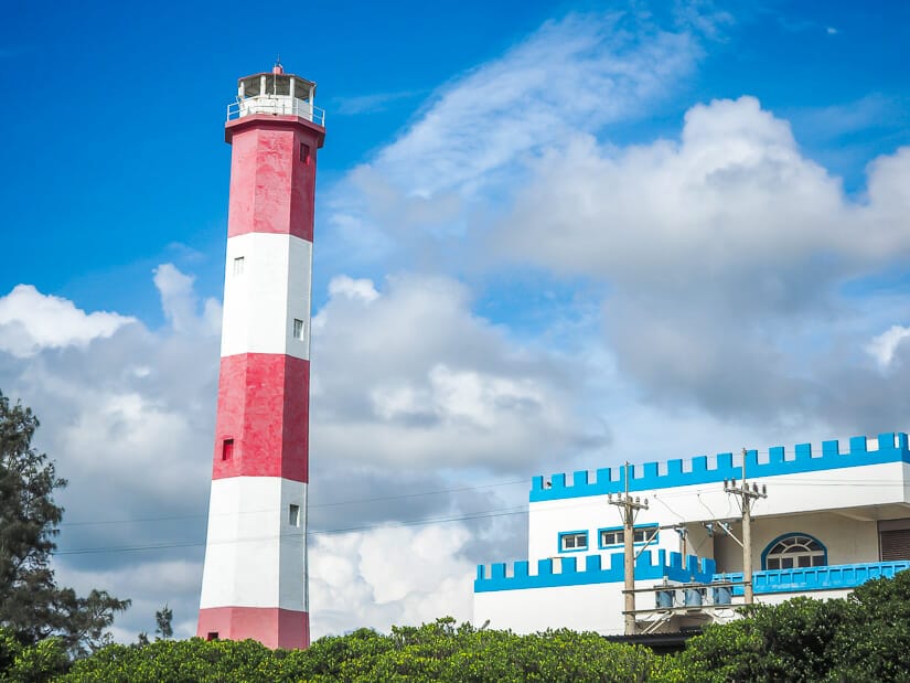 A red and white striped lighthouse and castle-like blue and white kindergarten beside it