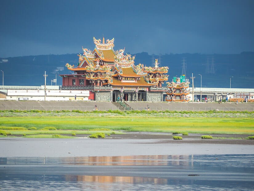 A large temple on the coast at Gaomei Wetlands, with some cyclists riding past it, and green grass along the beach in the foreground