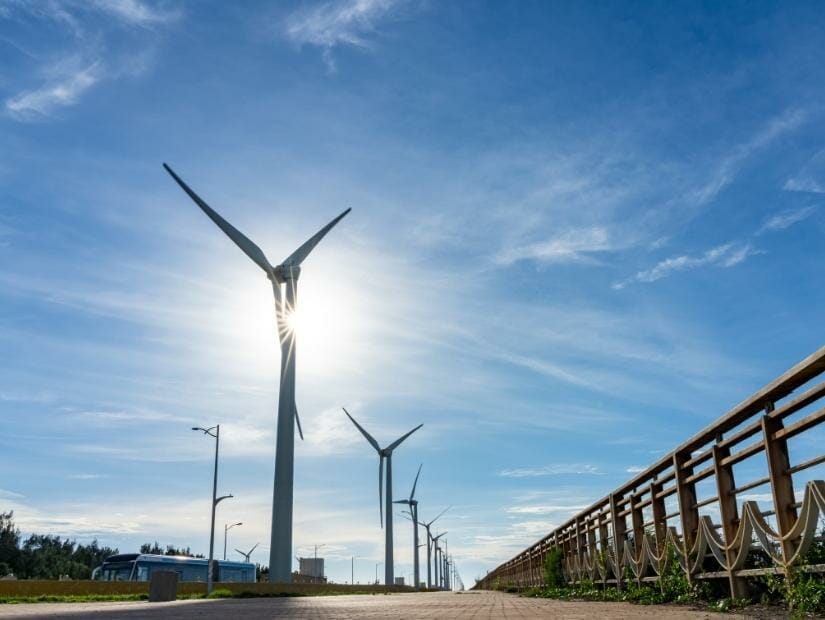 Looking up at a row of wind turbines at Gaomei from the level of the walking path, with the sun shining right behind one of the turbines