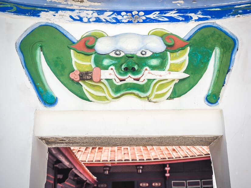An entrance to a traditional building with a painting of a lion holding a sword in its mouth painted above the door