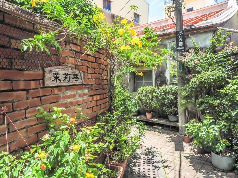 A narrow lane filled with plants that says the Chinese characters for Jasmine Lane on a brick wall