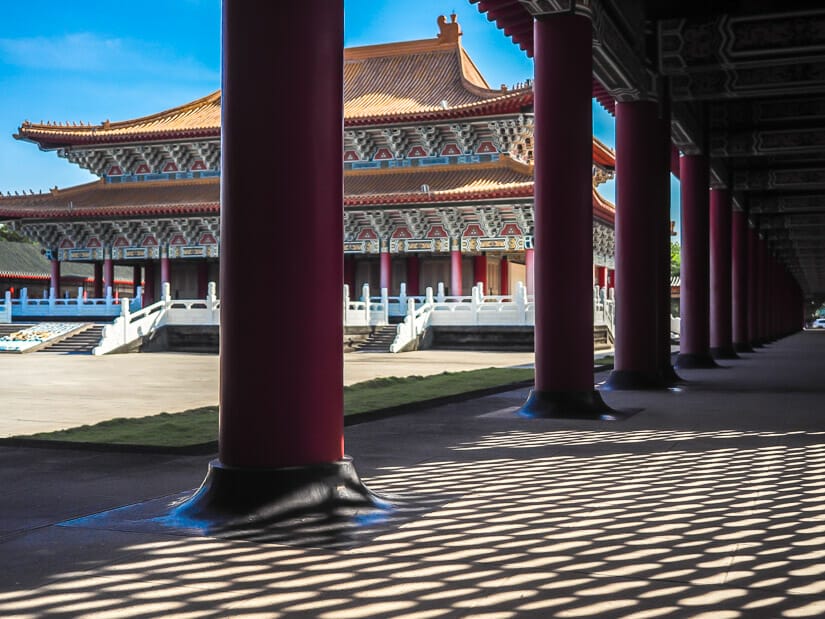 Some red columns and patchwork of shadows on the ground in the foreground and the Kaohsiung Zuoying Confucius temple in the background