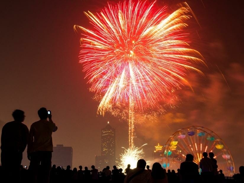 Some people standing watching fireworks with a Ferris wheel at Kaohsiung's Dream Mall below them