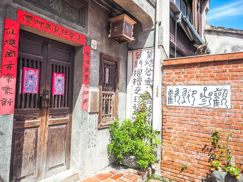 A house entrance with red Chinese couplets on the door and a red brick wall beside it, shot on Lukang Old Street