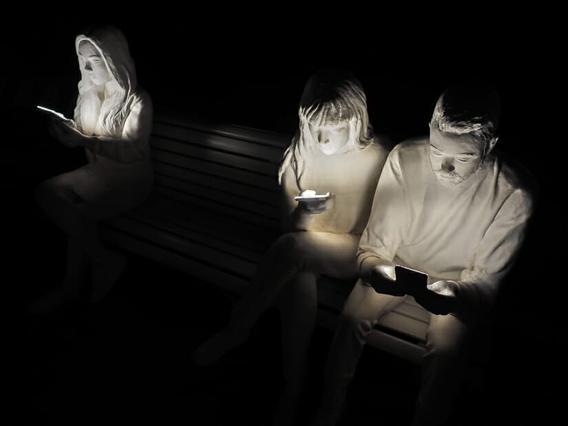 Three white statues looking at their cellphones in the dark, with the cell phone lights lighting up their faces, an art installation at Pier 2 Kaohsiung