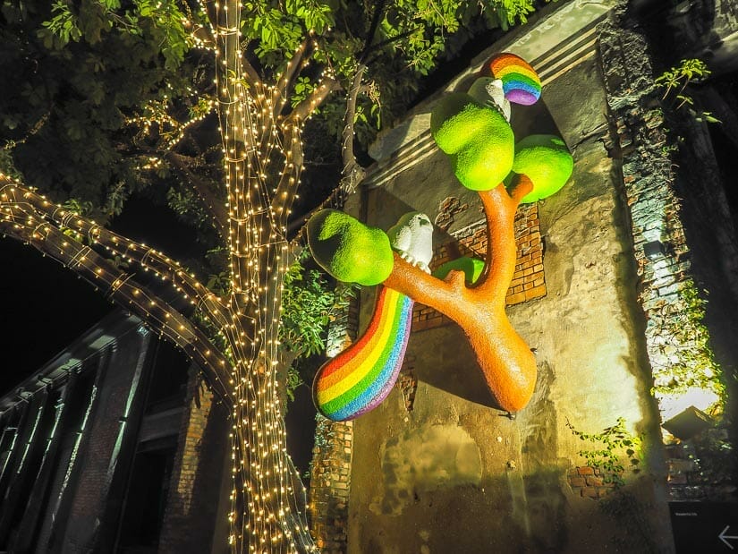 A colorful parrot statue on a tree on the side of a warehouse in Pier 2 Art Center at night