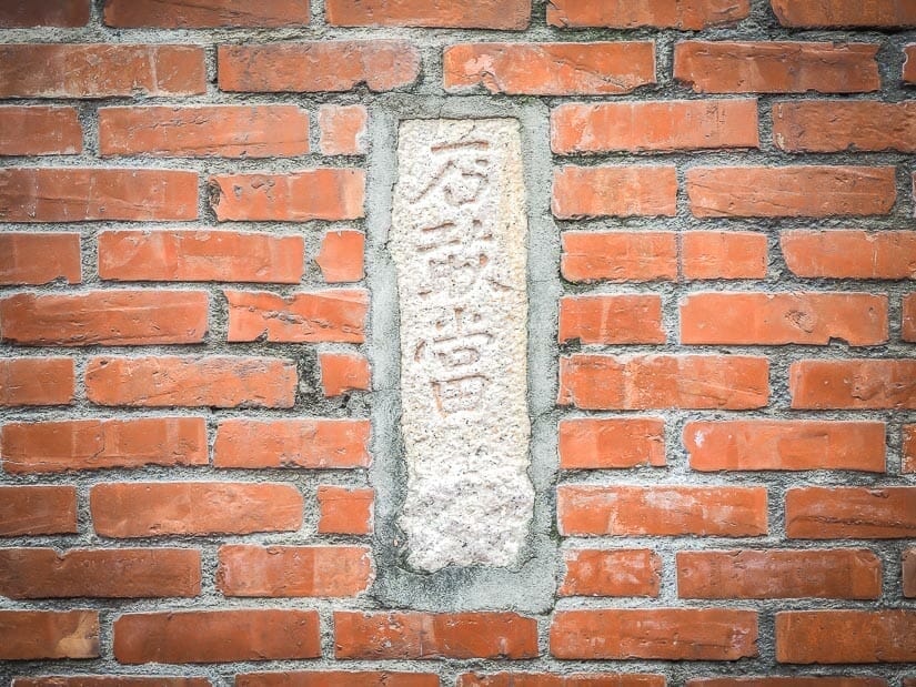 A grey stone with Mandarin characters on it inlaid in a red brick wall
