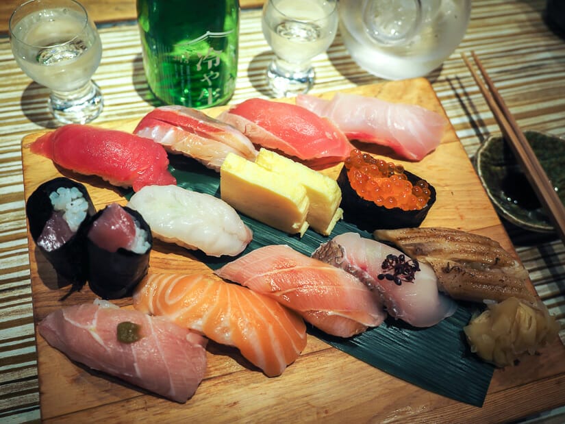 A wooden tray with about a dozen pieces of sushi on it at Addiction Aquatic Development, with some glasses of sake beside it