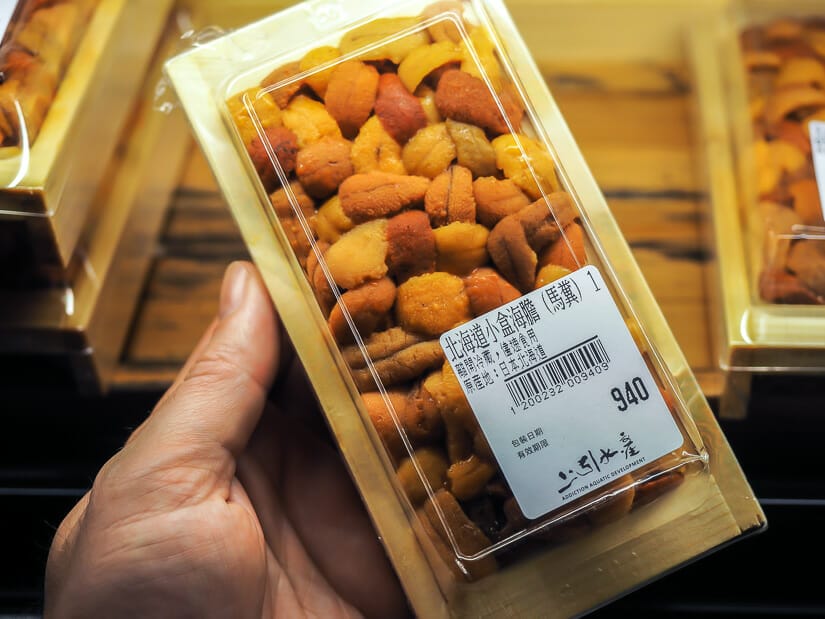 A hand holding up a take-away tray of fresh uni (sea urchin) for sale at Addiction Aquatic Development