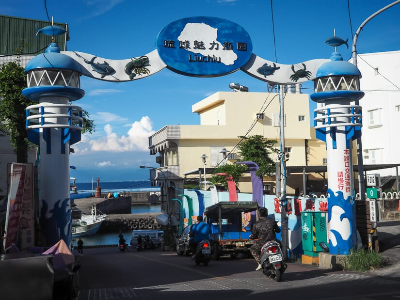 A scooter riding below a blue and white sign that says Liuchiu with the ocean in the background