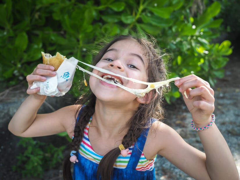 A kid stretching melted cheese from her hand to mouth from a fried cheese roll, a famous food on Xiaoliuqiu
