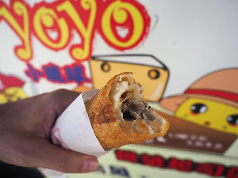 A hand holding up a cheese roll from a food vendor on Xiaoliuqiu