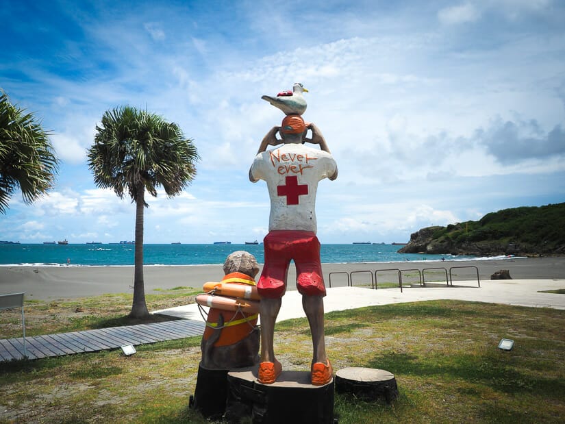 A statue of a life guard and a dog in a life jacket looking over Cijin Beach