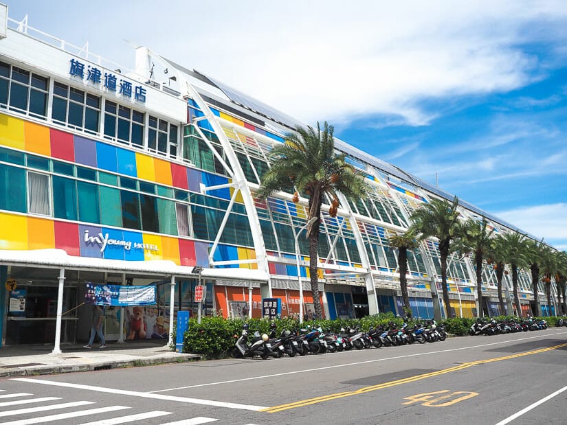 The colorful exterior of a hotel in Qijin, with palm trees along the street in front of it