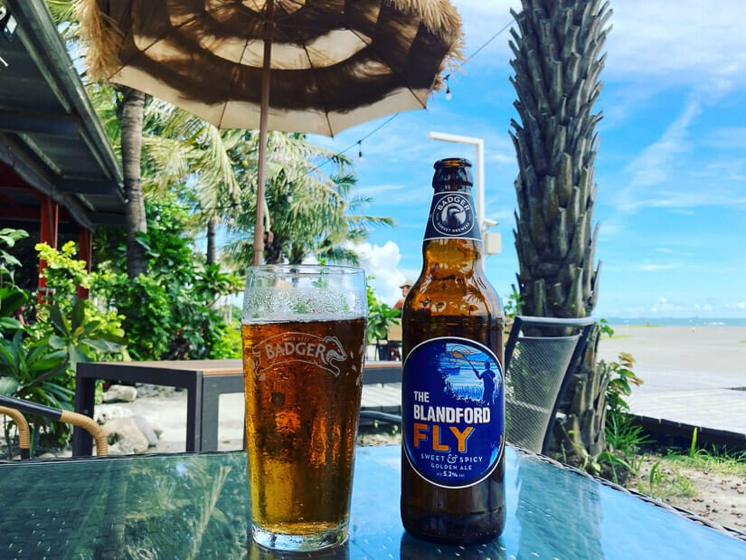 A bottle and glass of beer on a table at Cijin Sunset Bar with the a palm tree and Cijin Beach in the background