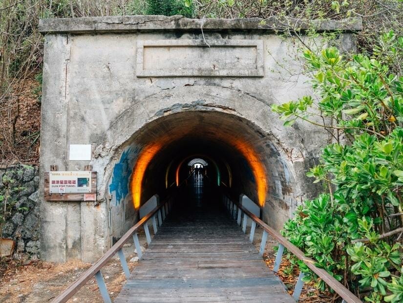 Looking into the dark Cijin Tunnel, with some colorful lights inside and silhouette of people walking through it