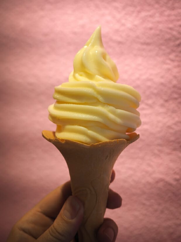 A hand holding up an orange colored soft ice cream cone from Iran Bazaar on Xiaoliuqiu