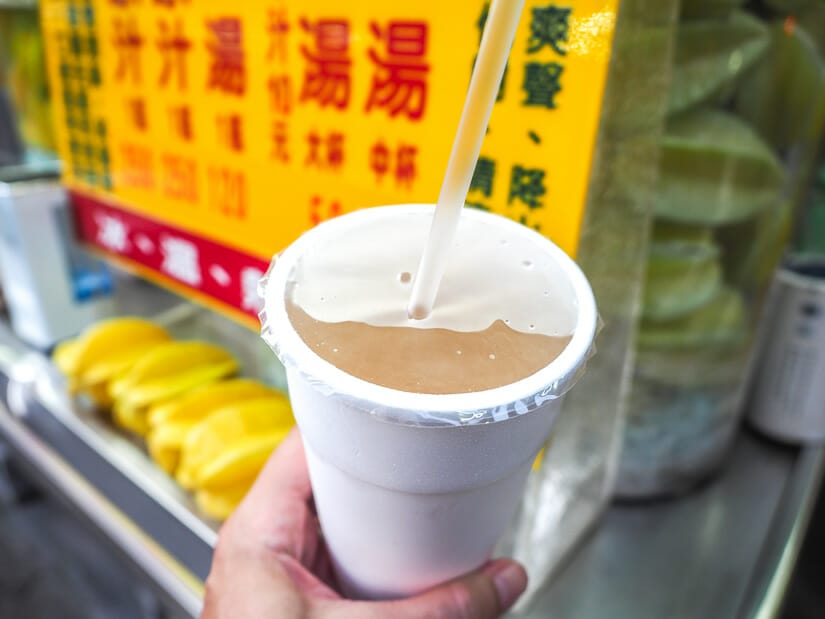 A cup hand holding a cup of star fruit juice with a a pile of starfruits on a drink stall in Zhonxiao Night Market Kaohsiung