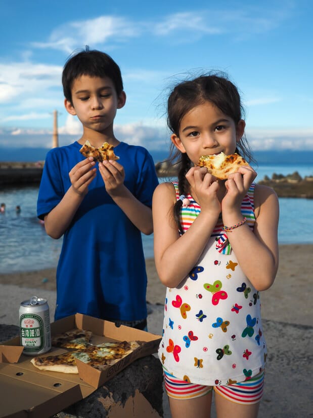Two kids eating pizza on the beach in Xiaoliuqiu