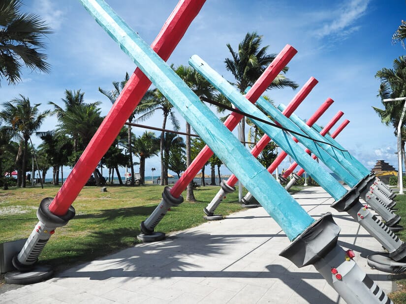 A sidewalk with rows of red and blue swords forming a canopy over it and leading to Cijin Beach