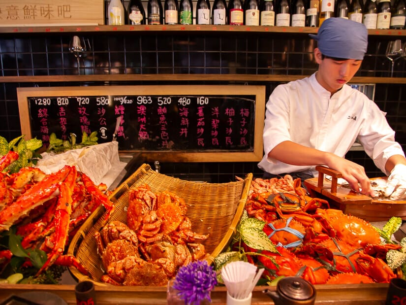 A chef preparing seafood with a pile of crabs in front of him at the Addiction Aquatic Development standing seafood bar
