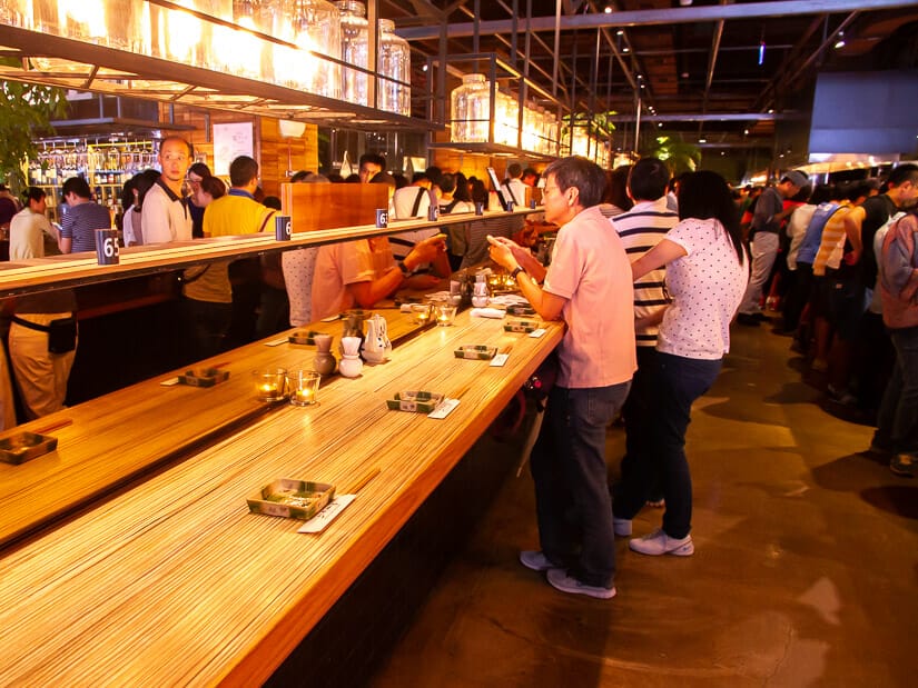 Some visitors standing up at a wooden sushi bar in Addiction Aquatic Development Taipei