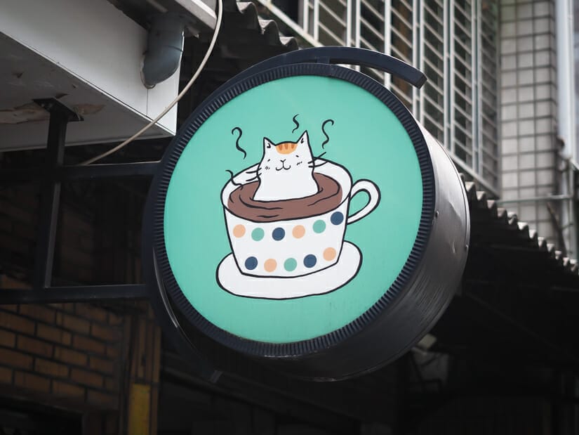 A cat cafe sign showing a car sitting in a cup of coffee