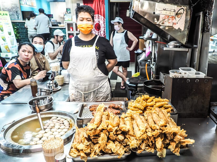 A Keelung Night Market vendor standing behind a pile of chicken rolls and fish ball soup
