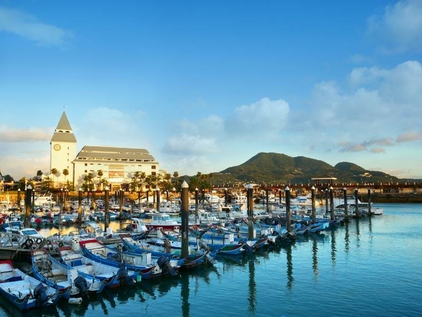 Several rows of boats docked at Fisherman's Wharf in Tamsui, with a building and mountain in the background