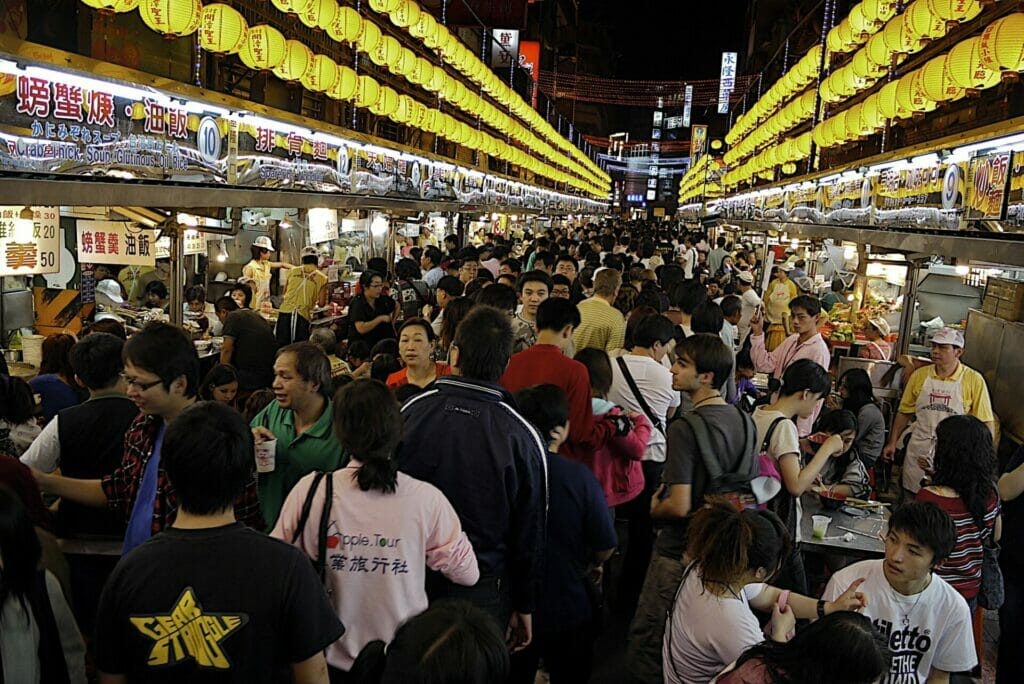 Crowds of people in Keelung Night Market, with yellow lanterns, and a white tourist looking back in the crowd