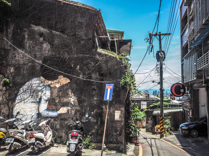 A narrow lane in Tamsui called Love Lane, with some scooters parked in front of a wall with painted mural on it