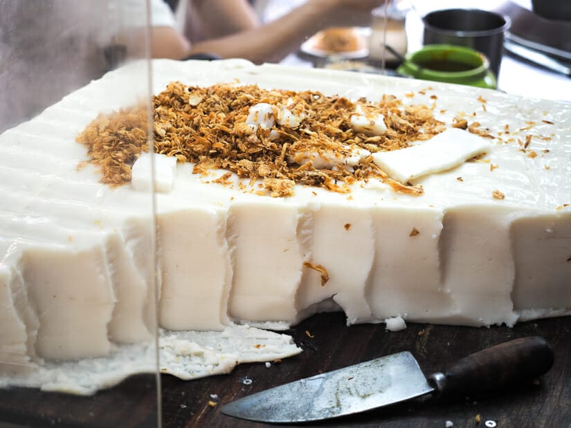 A huge oil cake on a food vendor stall in Keelung Night Market, with crispy fried shallots on top and a knfe on the side.