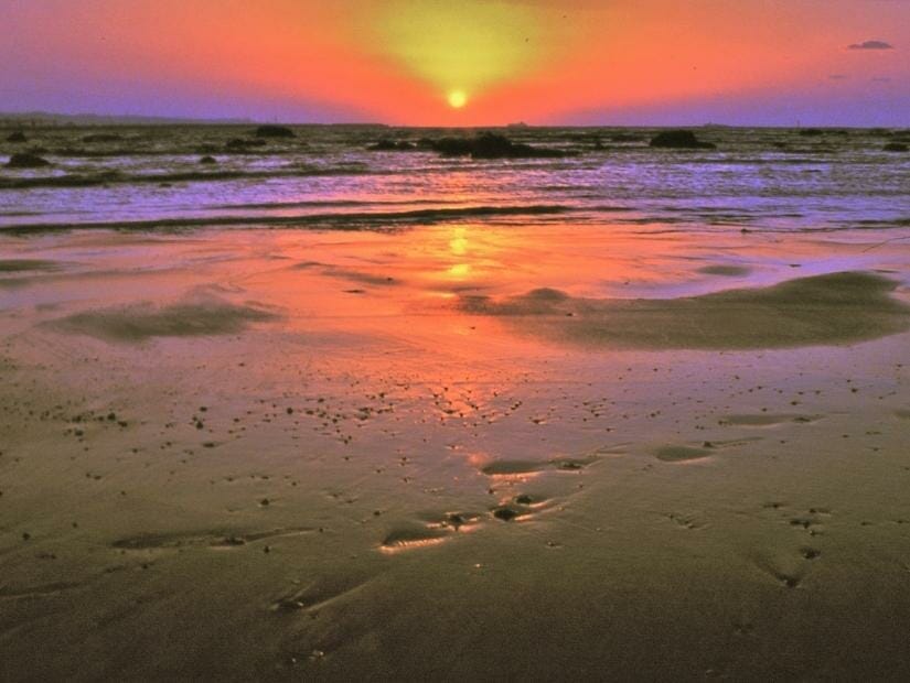 Close up of sand on Shalun Beach in Tamsui with waves and sun setting in background