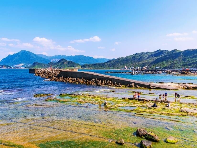 Some people exploring the coast at Badouzi in Keelung, with a long dock into the sea