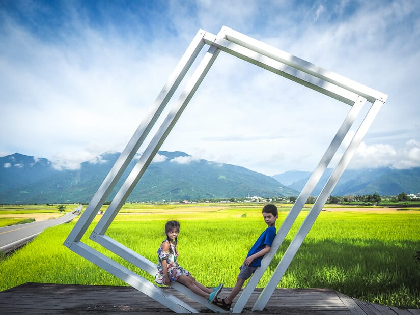 Two kids posing inside a large picture frame beside Mr. Brown Avenue in Chishang
