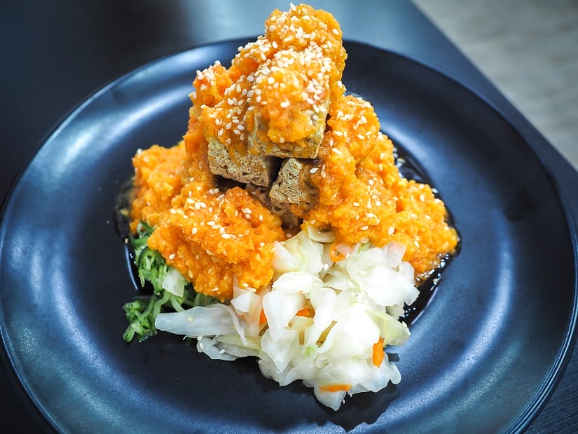 A black plate on a table with stinky tofu on it, with a mound of orange crab roe on top and pickled cabbage on the side