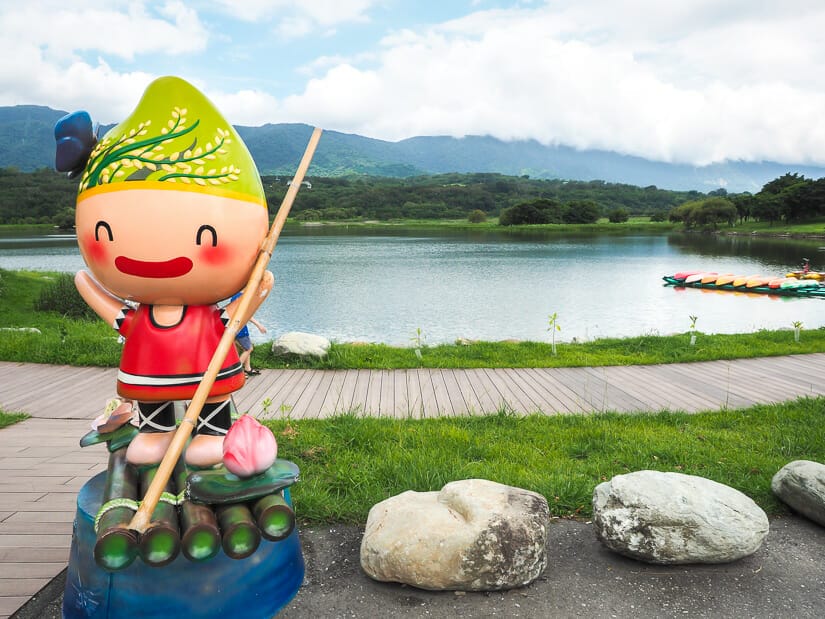 A colorful statue standing in front of Dapo Pond in Chishang, with a row of canoes on the lake