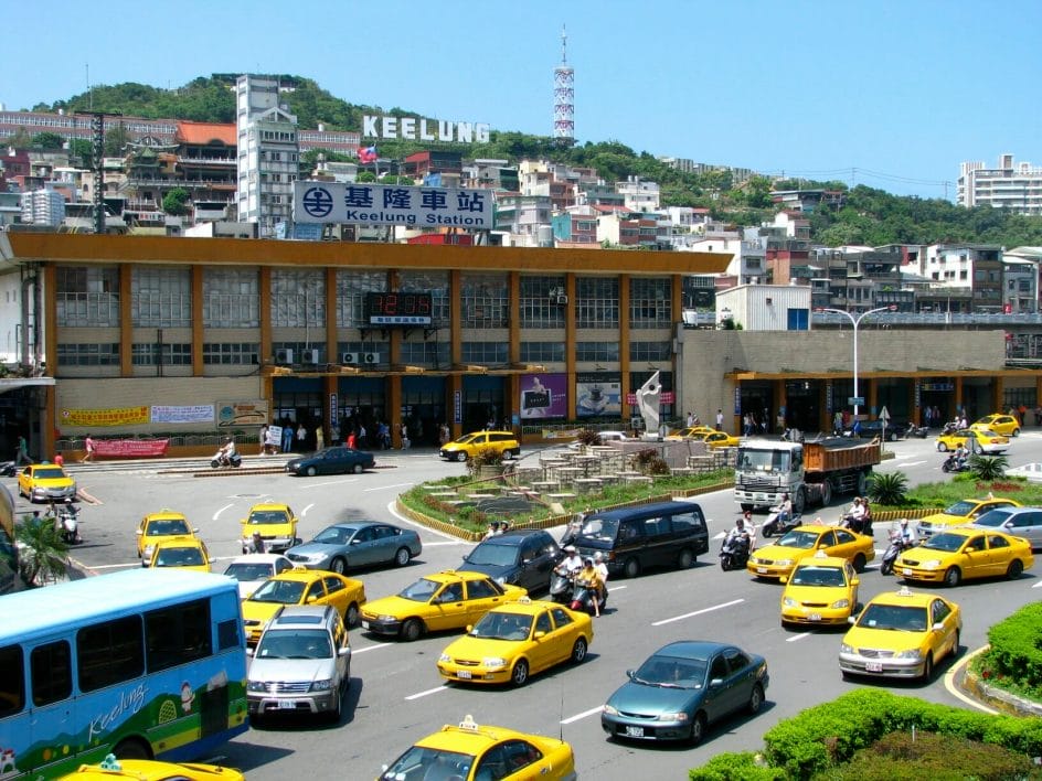An old image of Keelung train station before it was renovated, with Huzishan Keelung Landmark hollywood-style white letters Keelung sign visible above it and lots of taxis in front