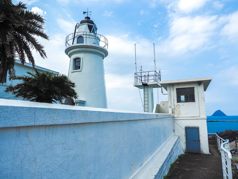 A white side wall and tower of Keelung Lighthouse, with Keelung Islet in the distance