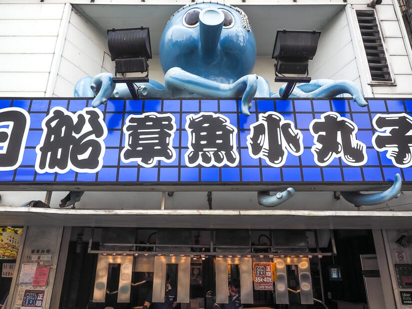 A takoyaki food stall in Feng Chia Night Market with a blue sign and huge blue statue of an octopus over it