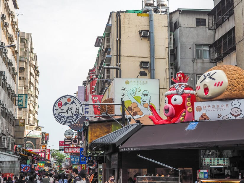 Looking down into Yizhong Street Night Market Taichung, with a huge octopus and puff ball statue on top of a building on the right and crowds of people