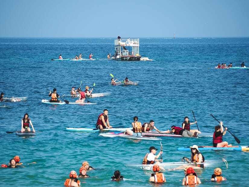 A crowd of taiwanese people swimming, kayaking, and doing other water sports at Aimen beach, the most popular beach in Penghu