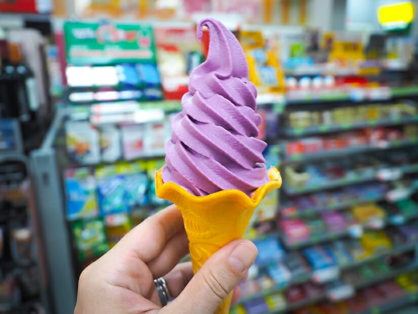 A hand holding up a purple cactus flavored soft serve ice cream cone at a convenience store in Penghu