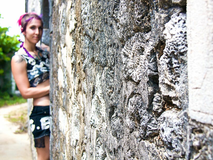 A girl with bright pink and purple hair standing beside a house made of coral on Penghu
