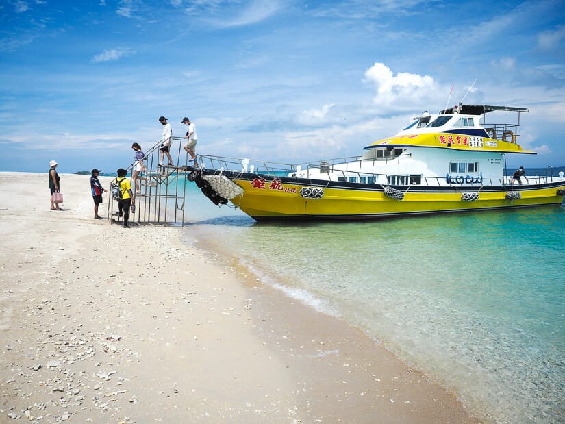 Some tourists getting off a yellow and white boat and climbing a ladder down onto a white-sand beach in Penghu called Peng Peng Beach