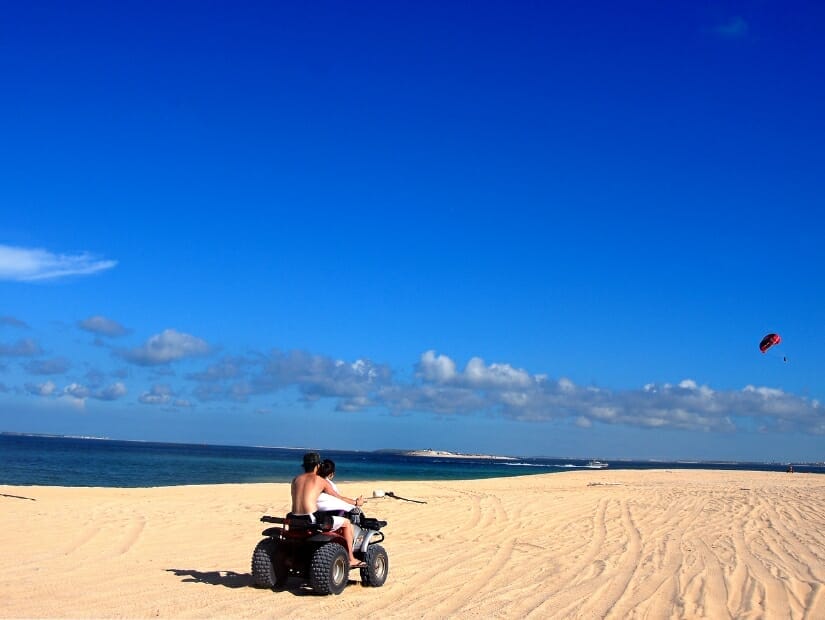 A couple riding an ATV on the sand on Jibei Island, with someone parachuting in the sky