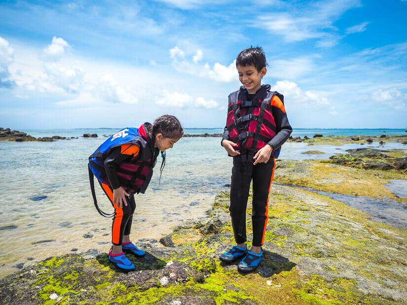 Two kids standing on the shore in Penghu and wearing wetsuits for snorkelling