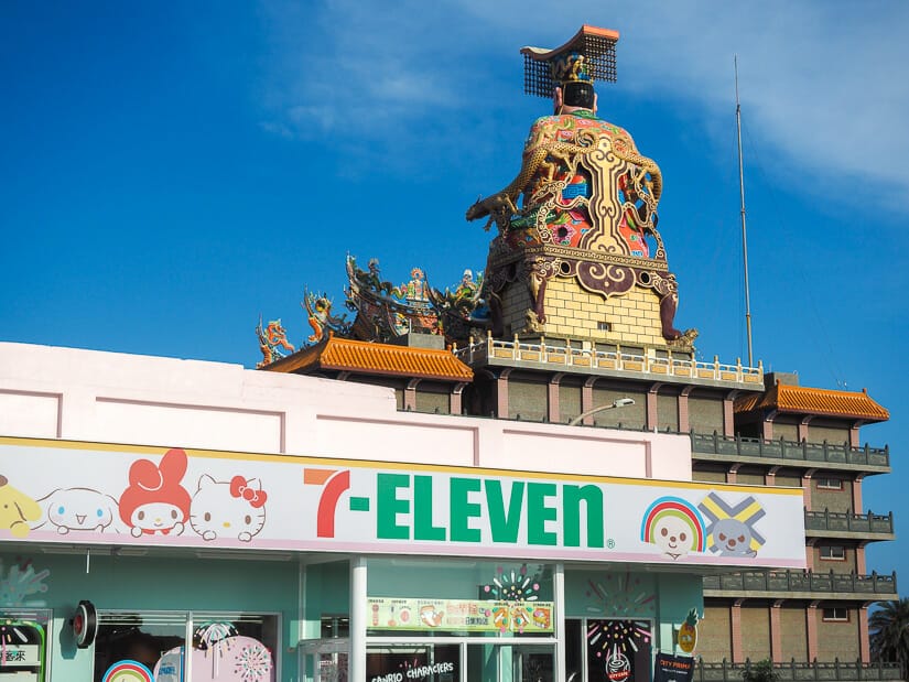 A 7-11 in Penghu with cute cats on the sign and huge statue on a temple behind it