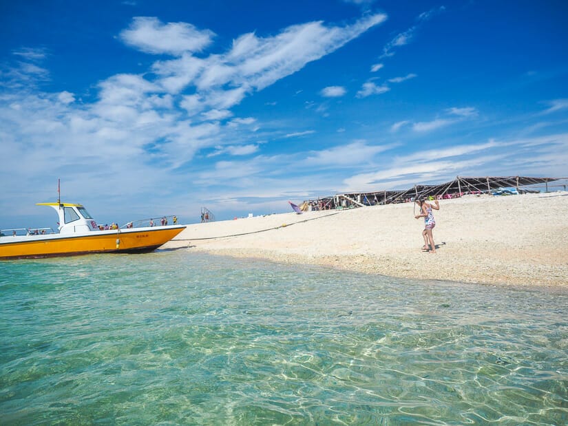 A girl walking on white sand Pengpeng Beach in Penghu with a boat on the side and very clear water