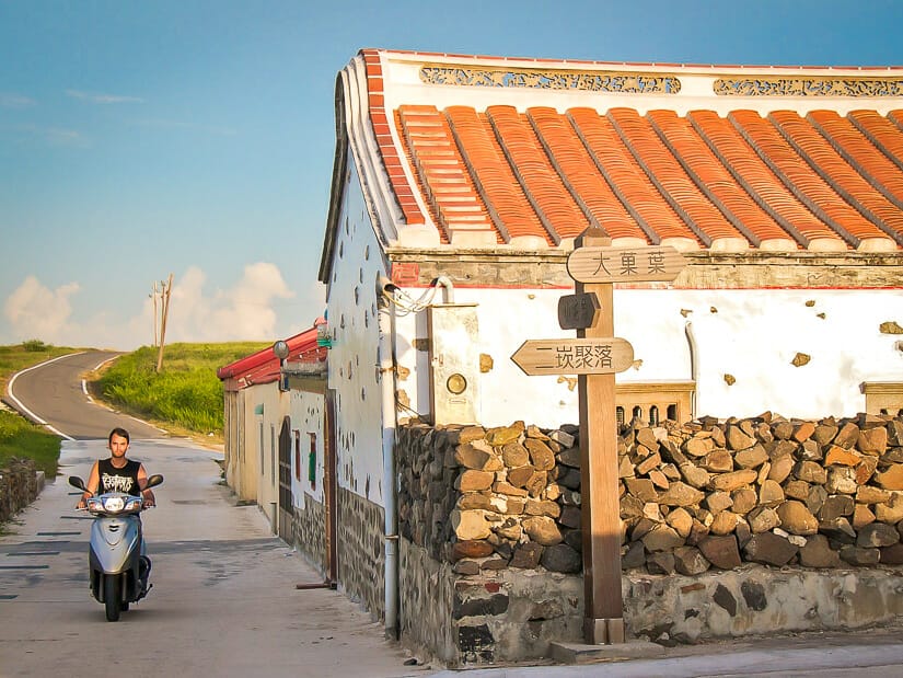 A man riding a scooter past an old house in Erkan Historical Village Penghu